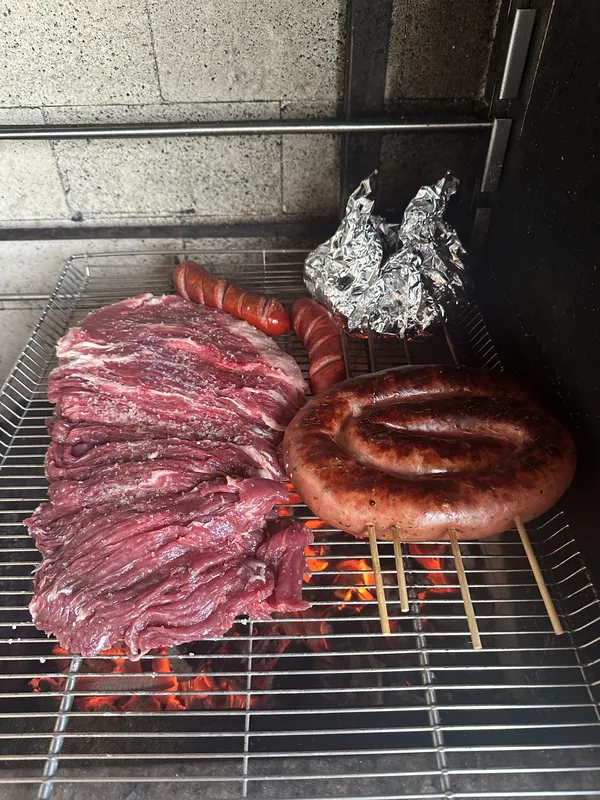 Assorted meats and sausages cooking over charcoal